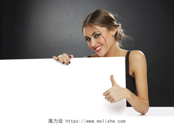 微笑着的年轻女子拿着空白的白色广告旗帜和给了深色背景招牌拇指